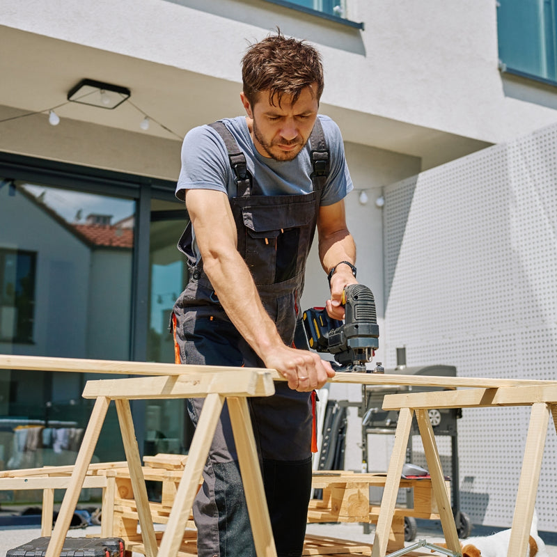 Man using a power drill on a wooden project outdoors.